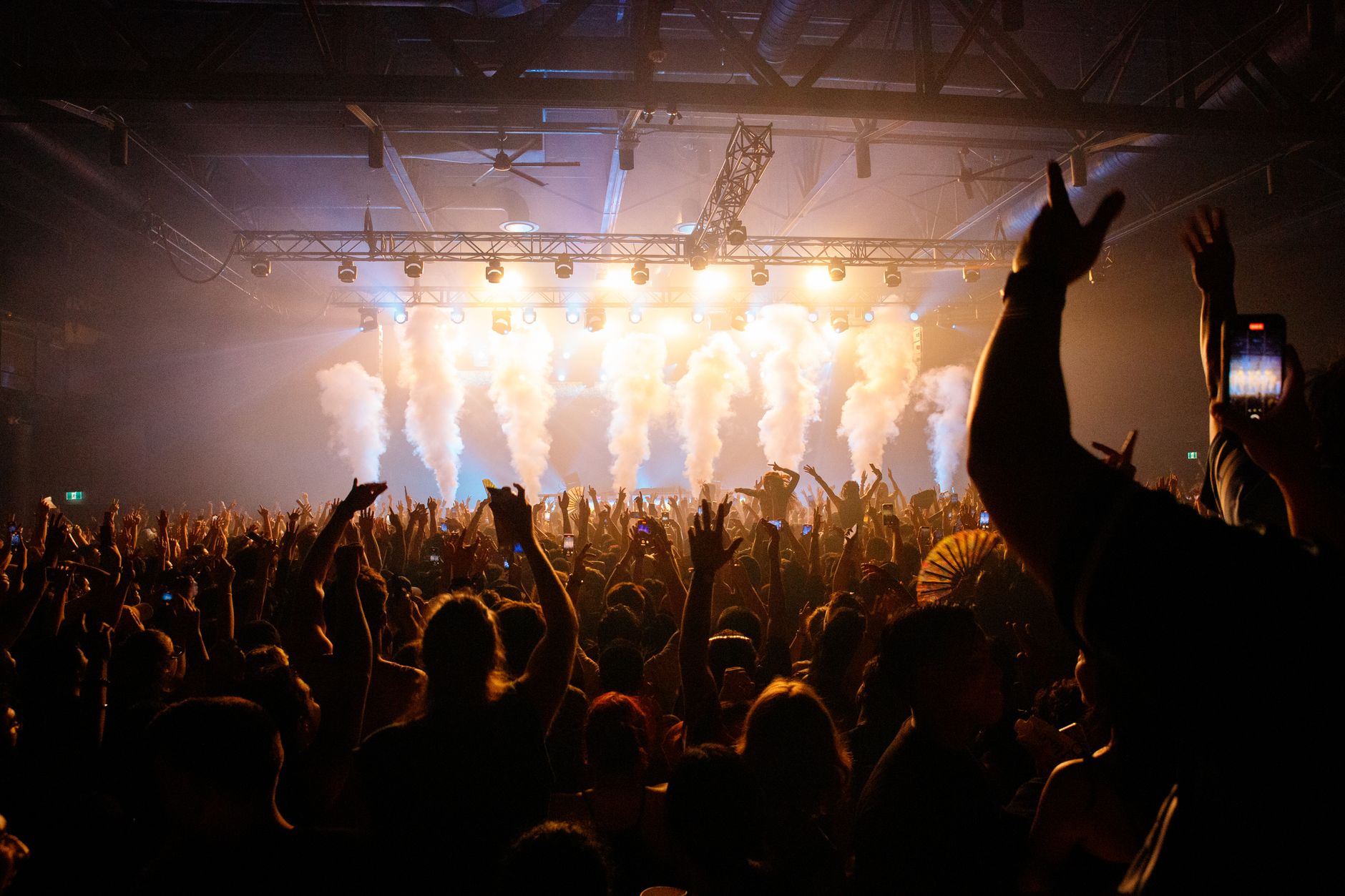 An arena concert crowd under stage lighting and smoke effects.