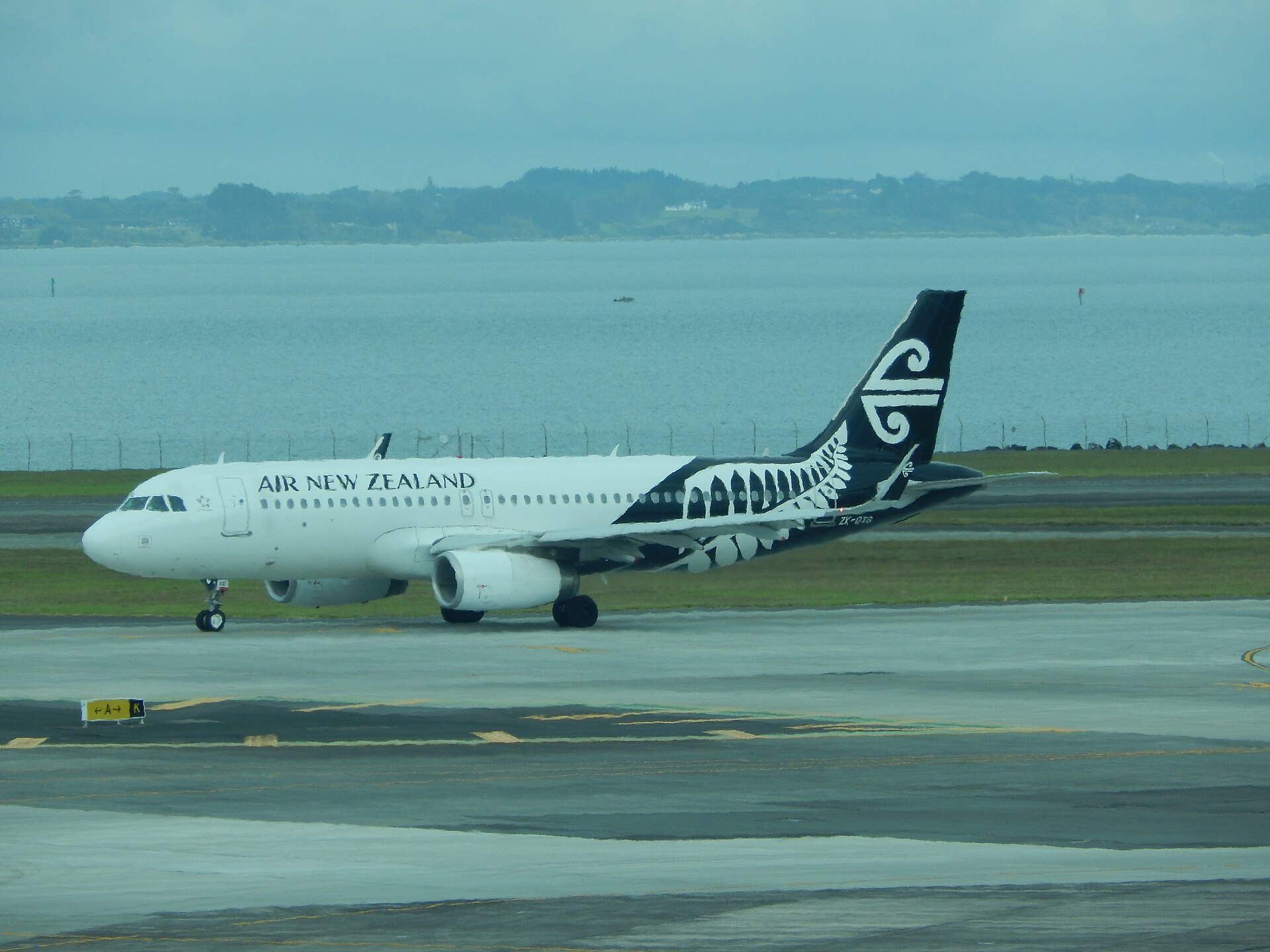 An Air New Zealand Airbus A320 taxiing at Auckland Airport with the Manukau Harbour behind it