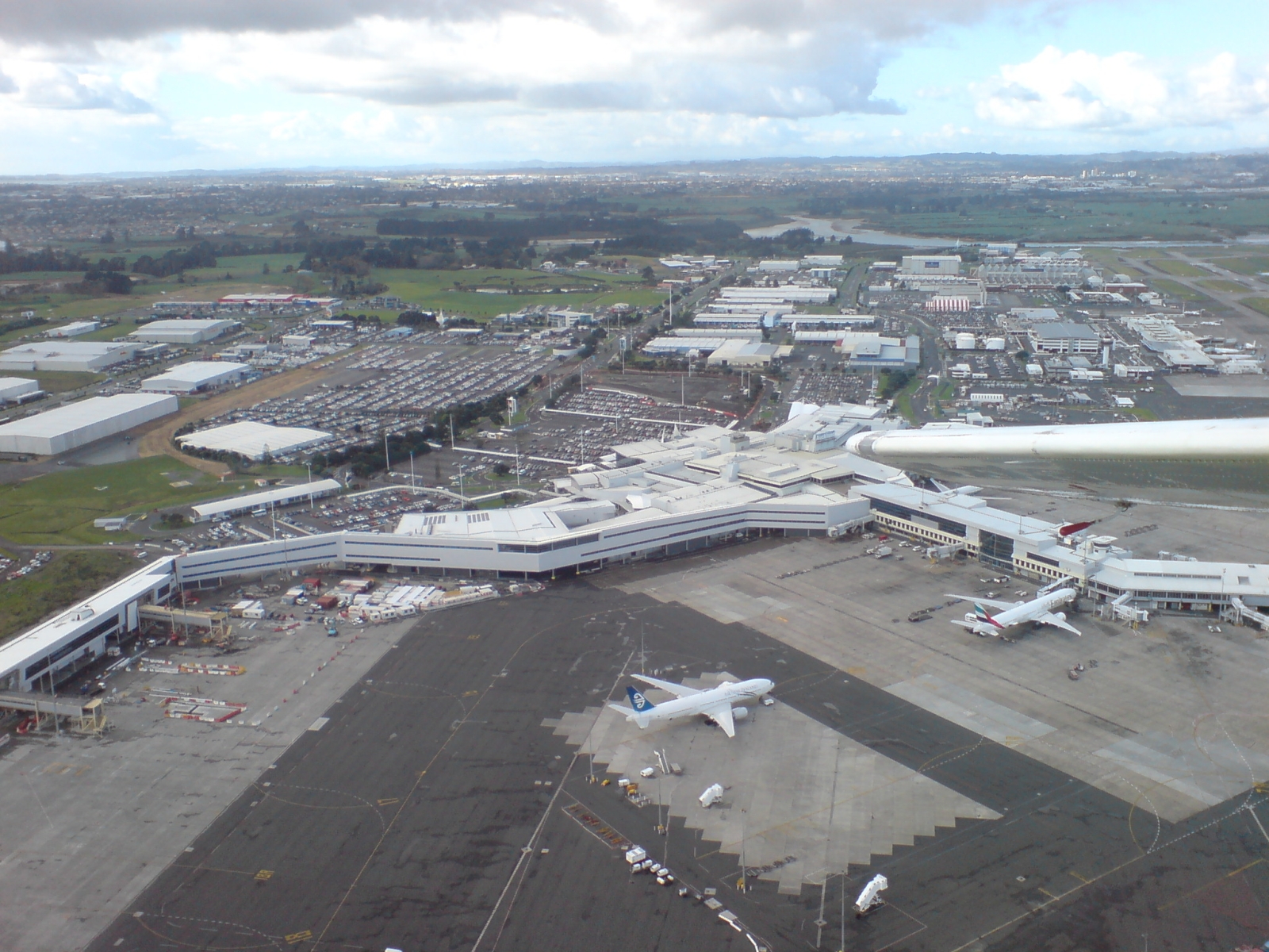 Aerial view of Auckland Airport showing the terminal buildings surrounded by vast open-air car parks