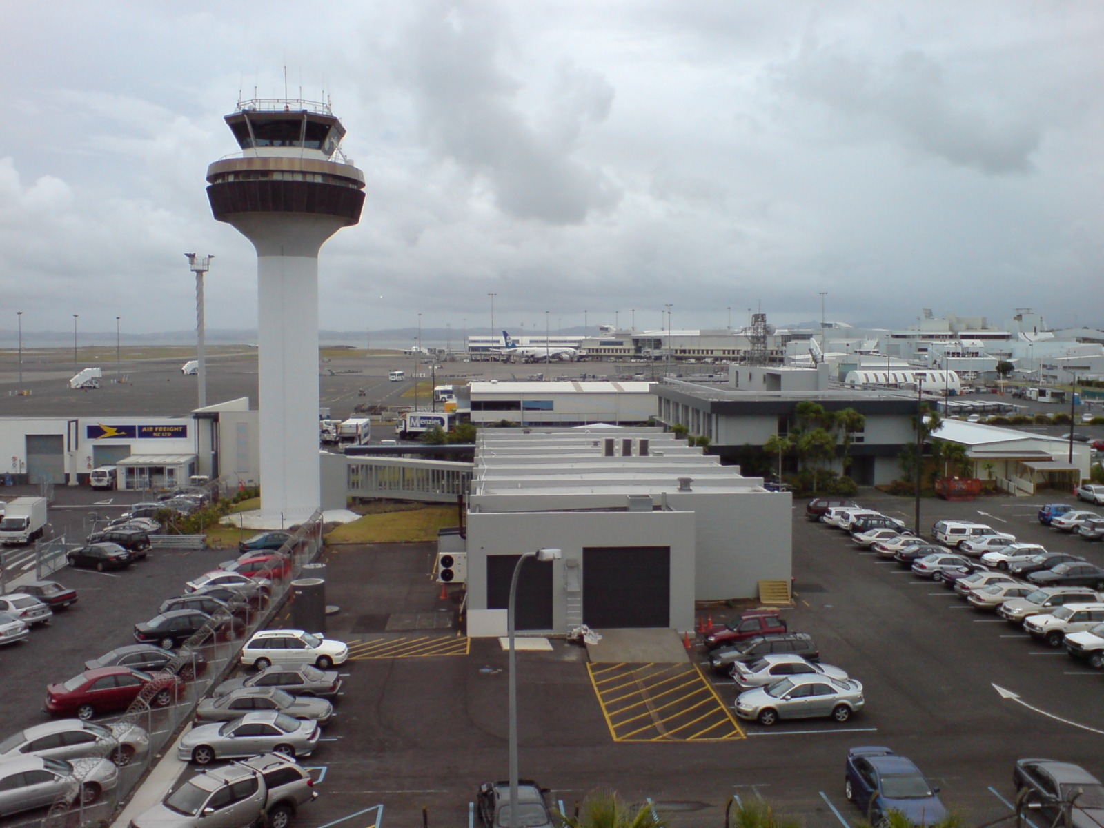 Auckland Airport's control tower above the apron, with parked aircraft and rows of car parking in the foreground