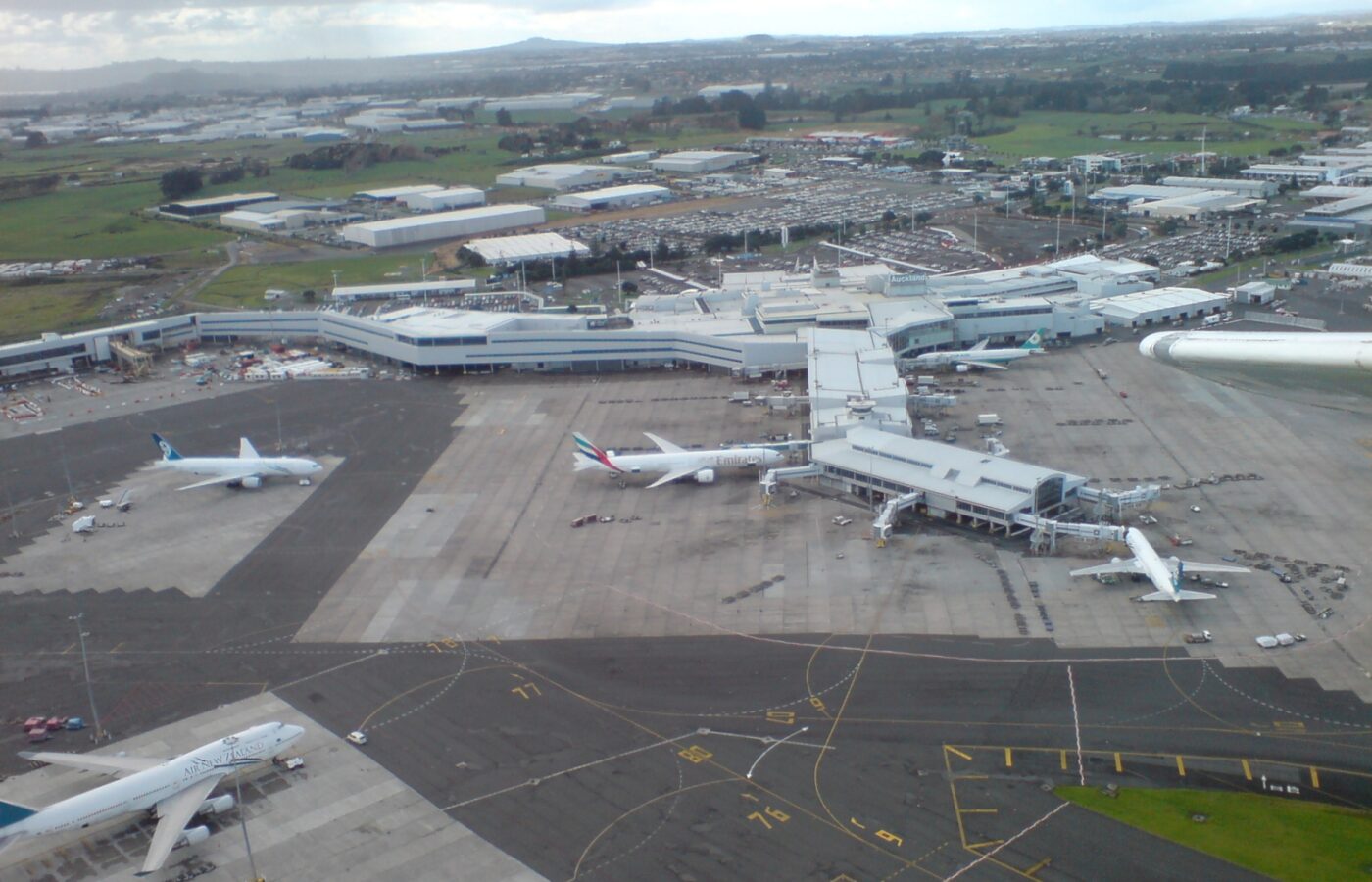 Aerial view of Auckland Airport's international terminal, apron and parked widebody aircraft with Manukau industrial land beyond