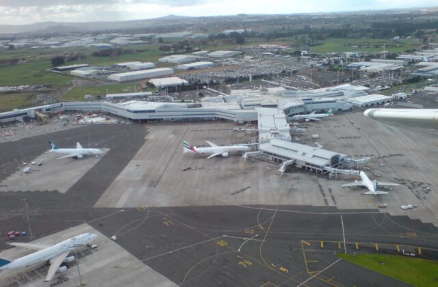 Aerial view of Auckland Airport's international terminal, apron and parked widebody aircraft with Manukau industrial land beyond