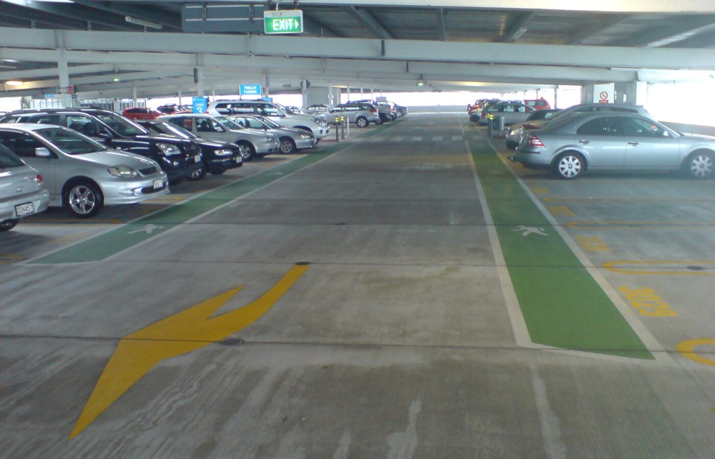 Inside the multi-storey car park at Auckland Airport, with parked cars, marked walkways and an exit sign