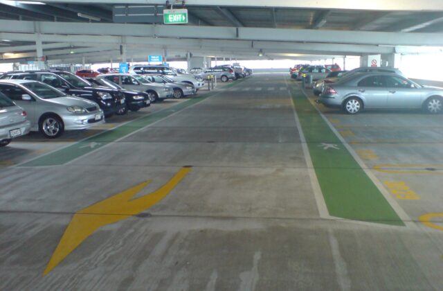 Inside the multi-storey car park at Auckland Airport, with parked cars, marked walkways and an exit sign
