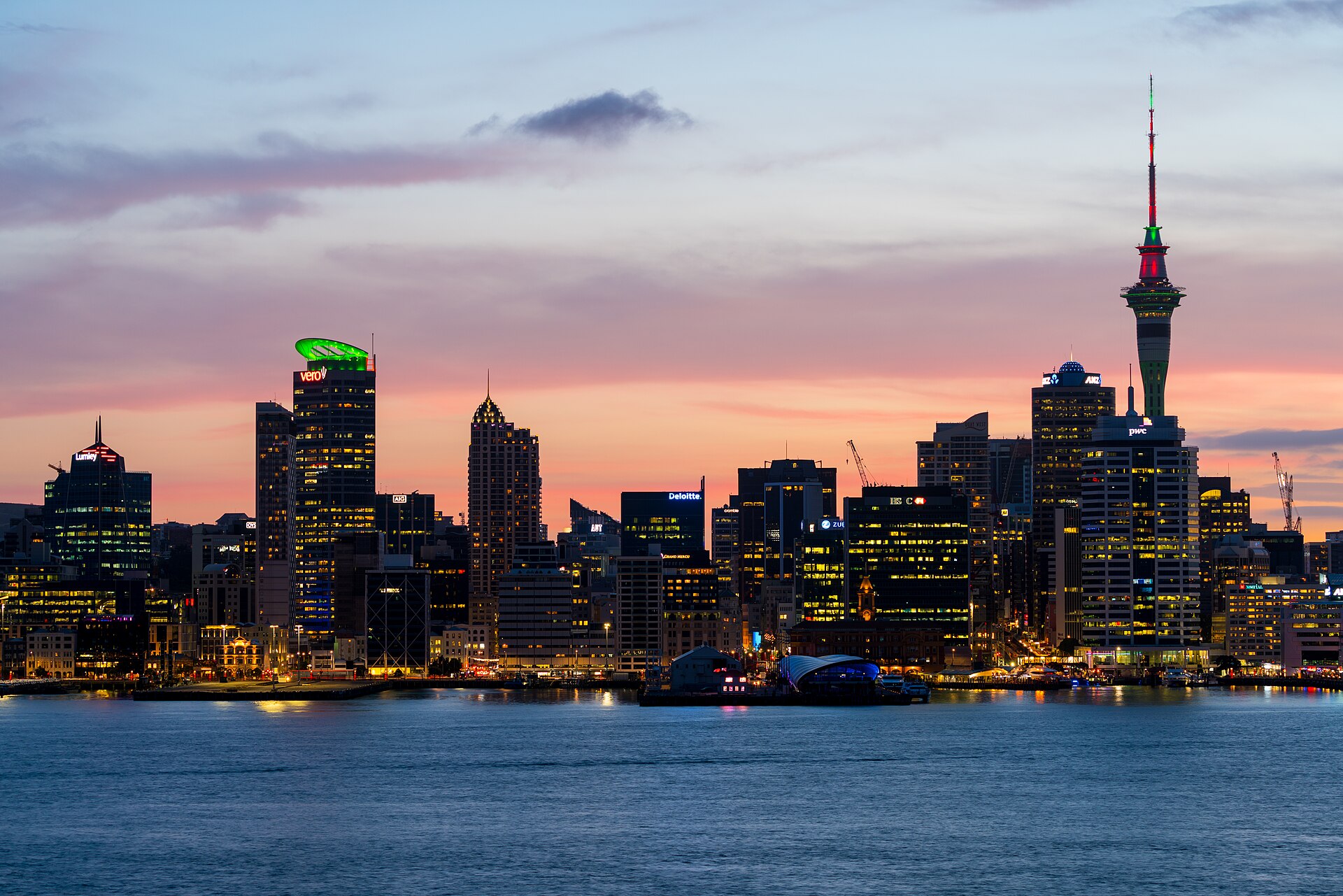 Auckland's city centre skyline at dusk across the Waitematā Harbour, with the Sky Tower lit