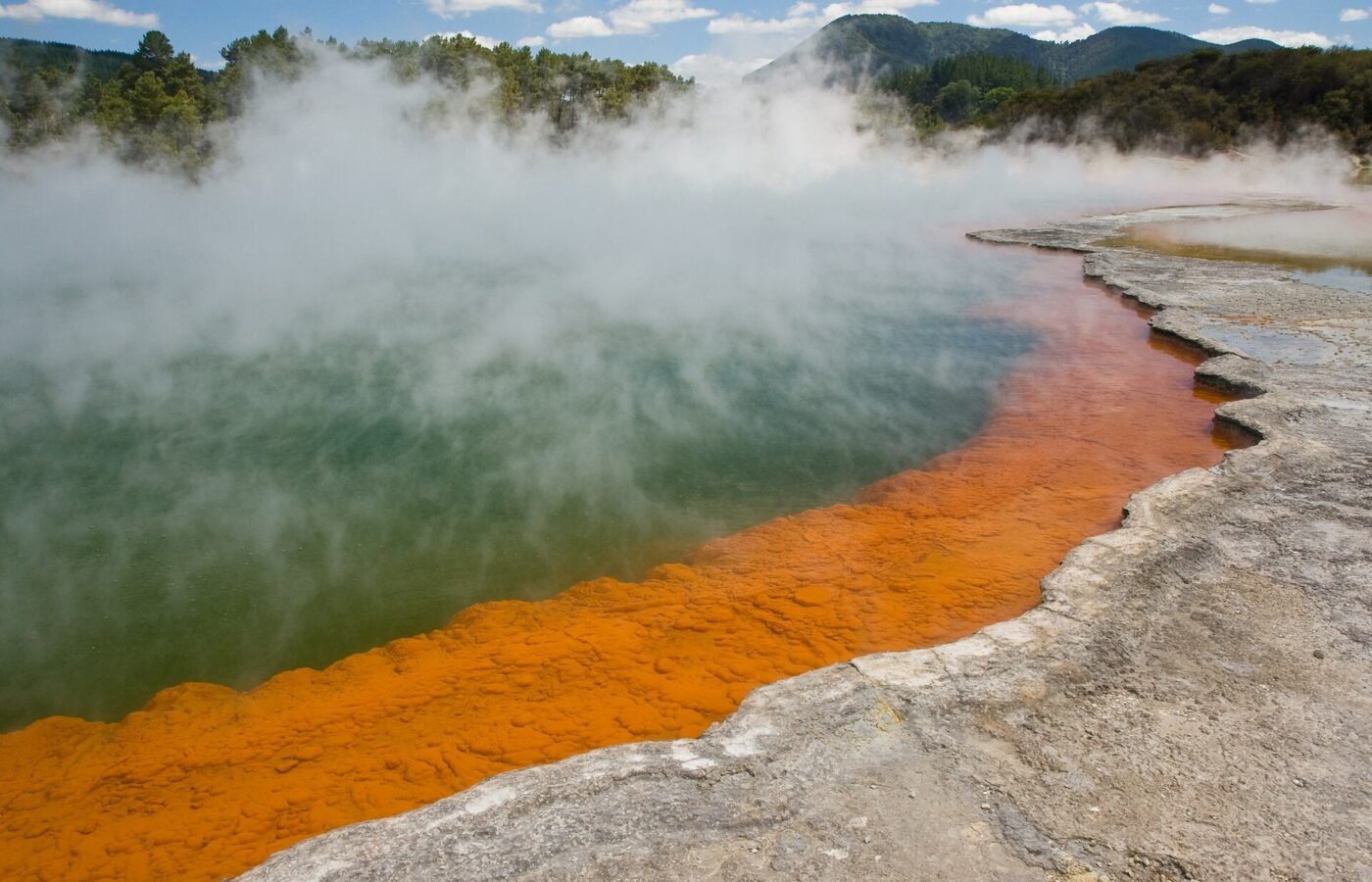 Steam rising off the green Champagne Pool at Wai-O-Tapu, its edge ringed with bright orange mineral deposits