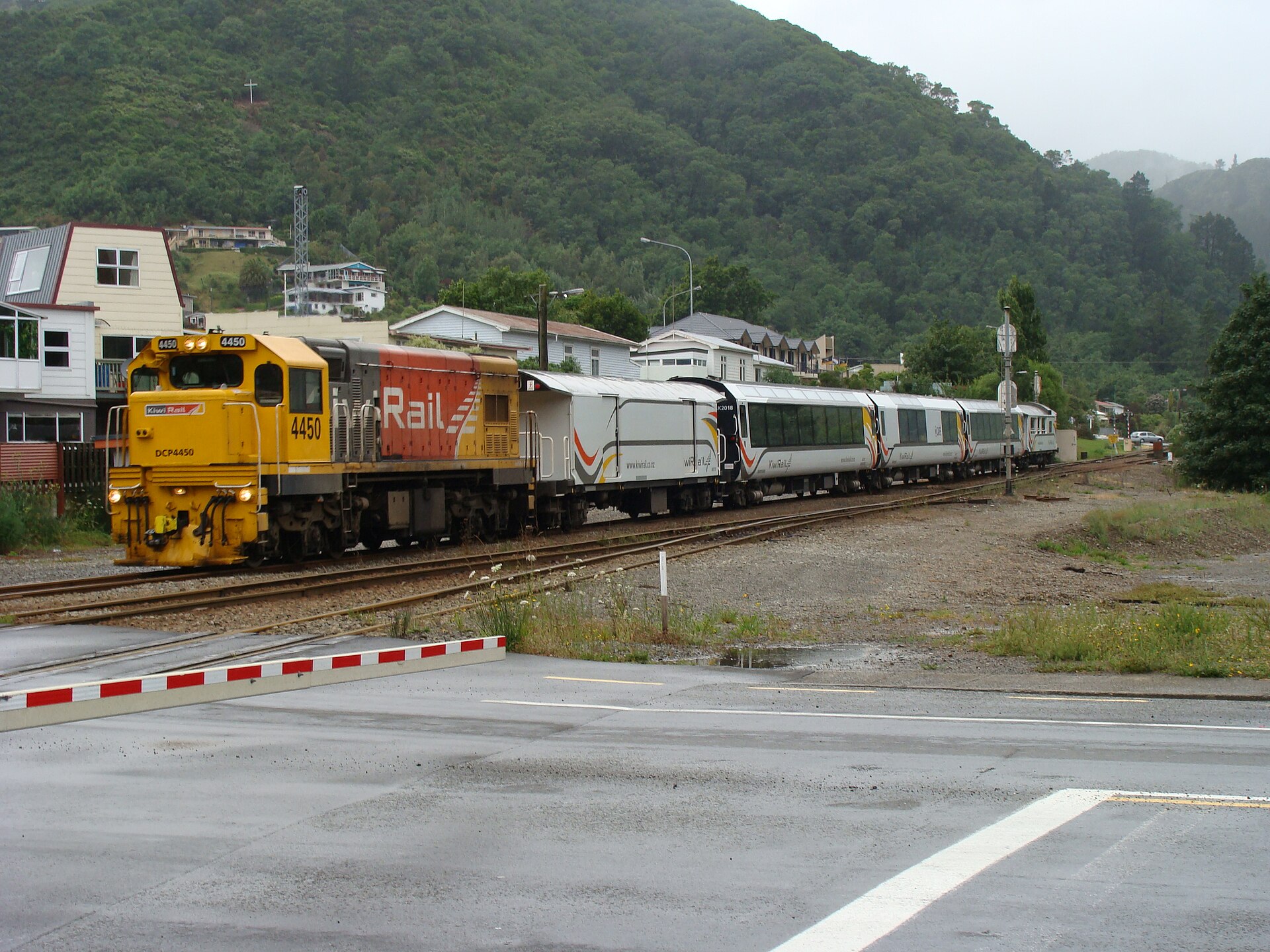 A KiwiRail locomotive hauling the Coastal Pacific's passenger carriages past houses and bush-covered hills