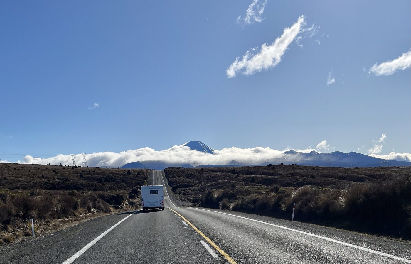 A campervan on the Desert Road through Tongariro National Park, with the volcanoes on the skyline under cloud