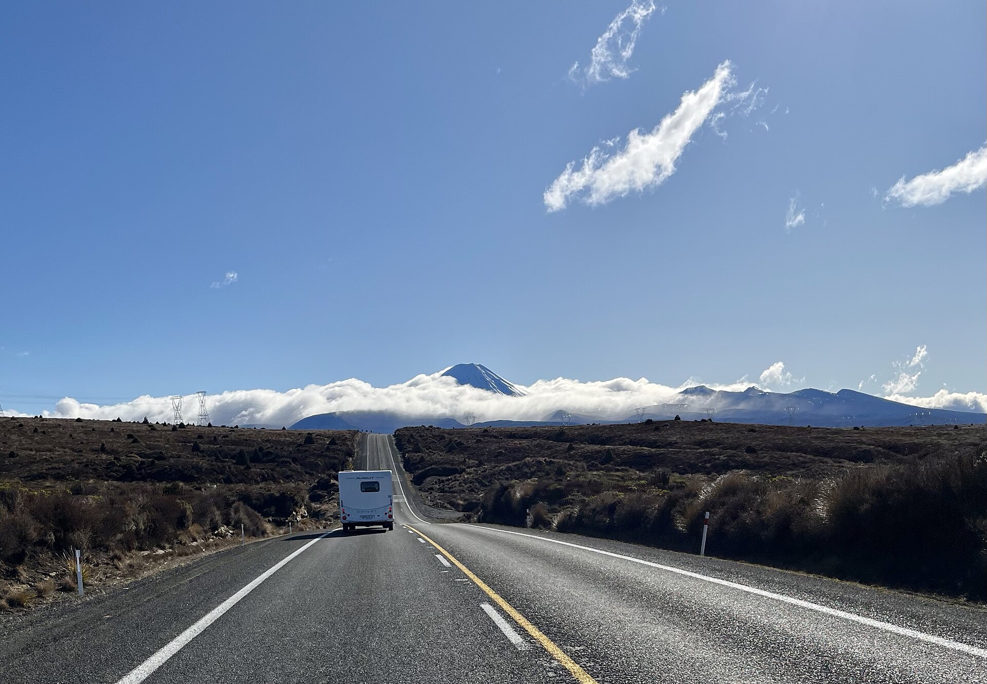 A campervan on the Desert Road through Tongariro National Park, with the volcanoes on the skyline under cloud