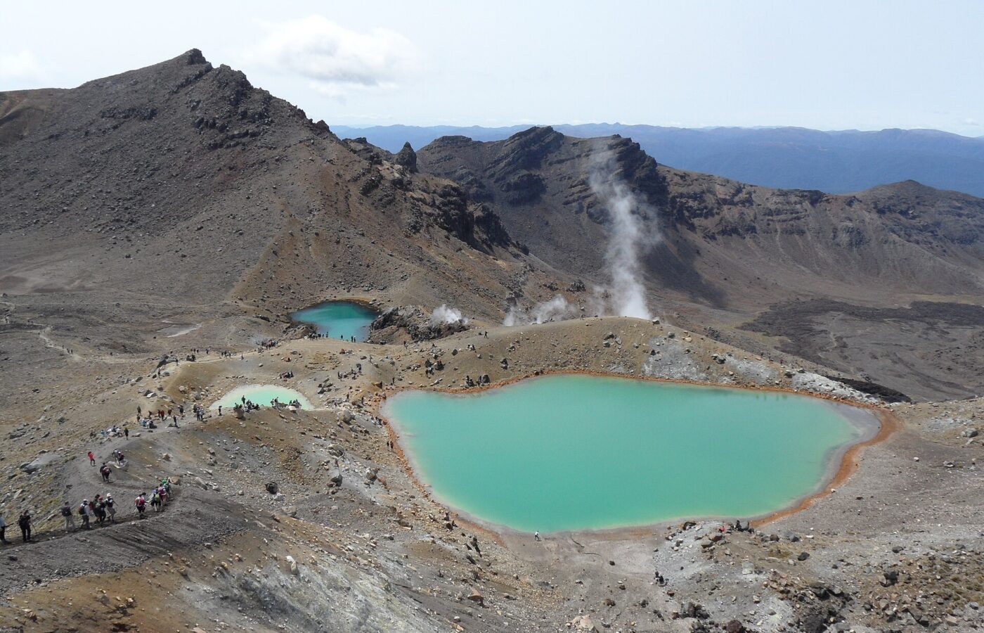 The milky-green Emerald Lakes below steaming, ochre volcanic slopes on the Tongariro Alpine Crossing, with walkers on the track