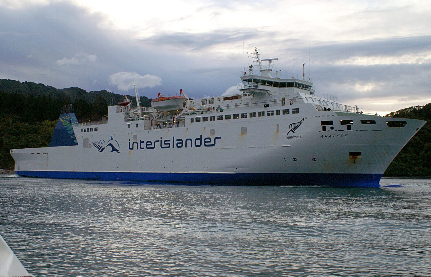 An Interislander ferry sailing through calm water between the bush-covered hills of the Marlborough Sounds