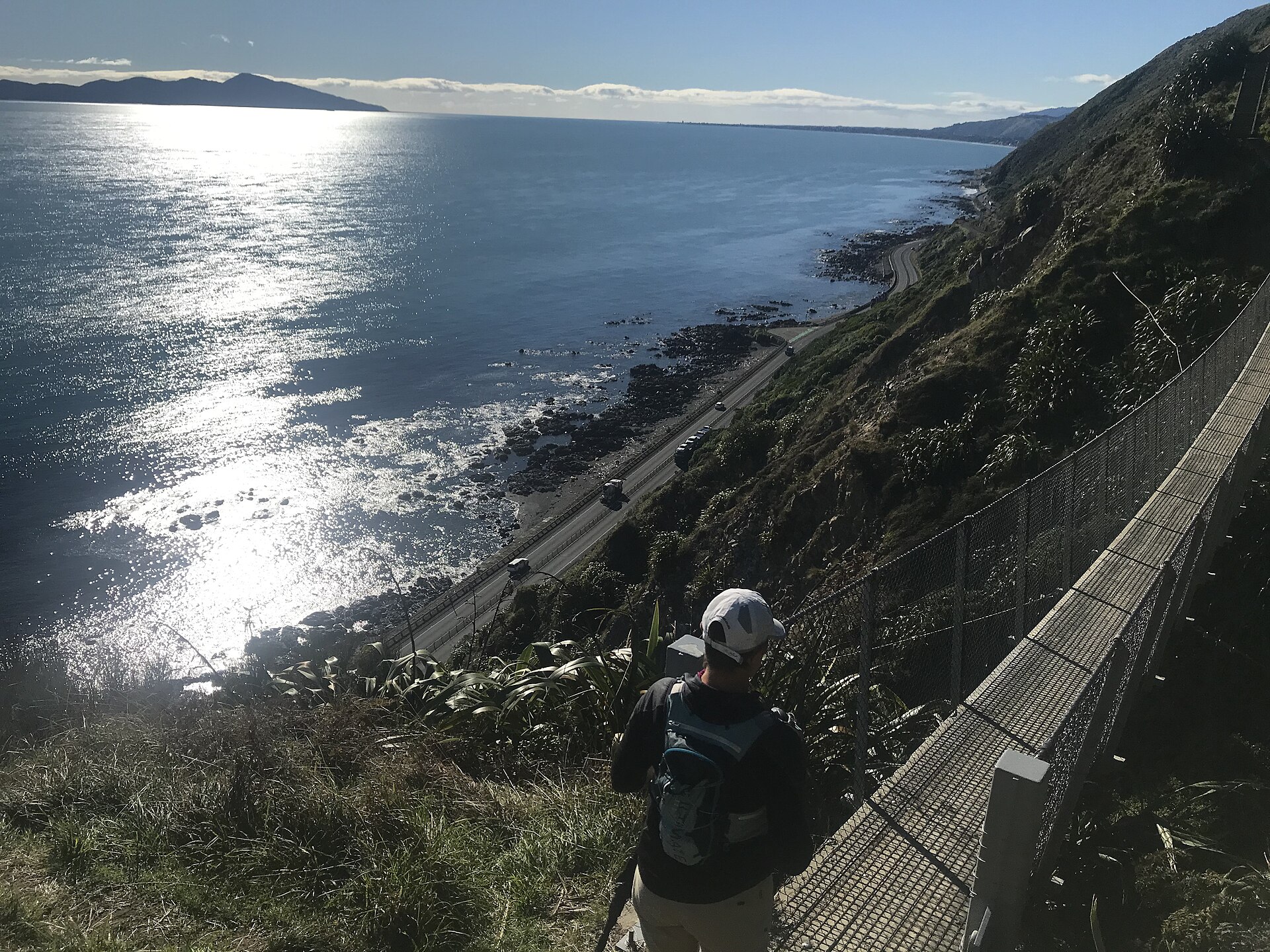 A walker on the Paekākāriki Escarpment Track high above the coast road and the sea, with Kāpiti Island in the distance