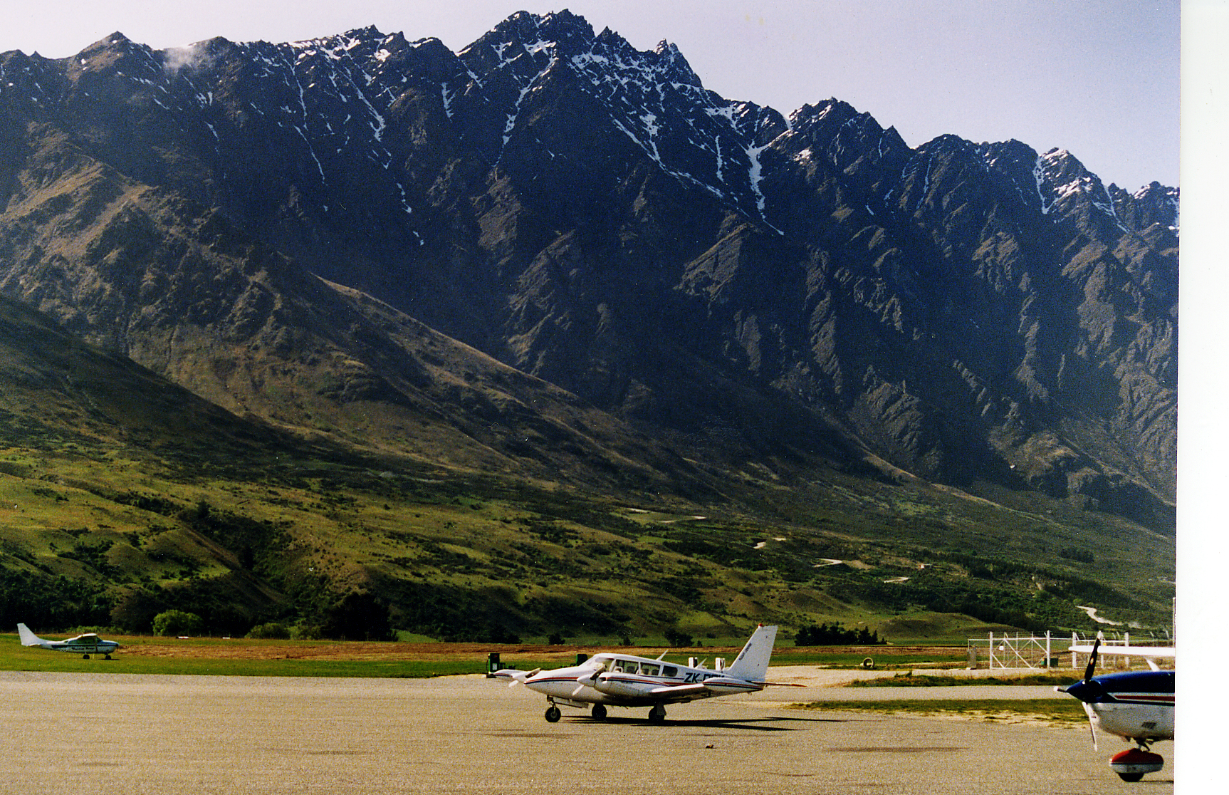 Small aircraft parked on the apron at Queenstown Airport below the jagged, snow-streaked peaks of the Remarkables