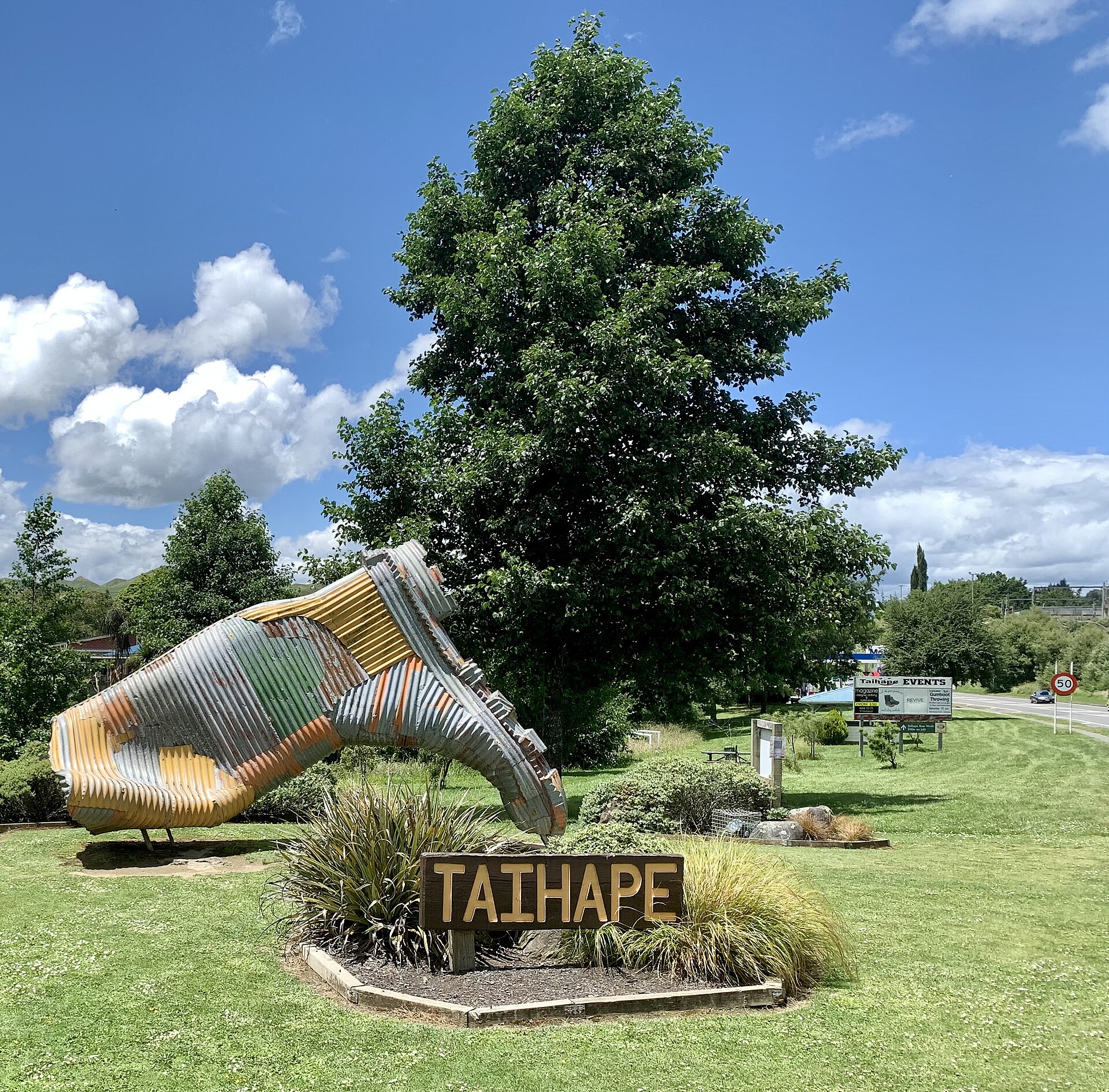 The giant corrugated-iron gumboot sculpture beside a Taihape sign on a grassy verge under a blue sky