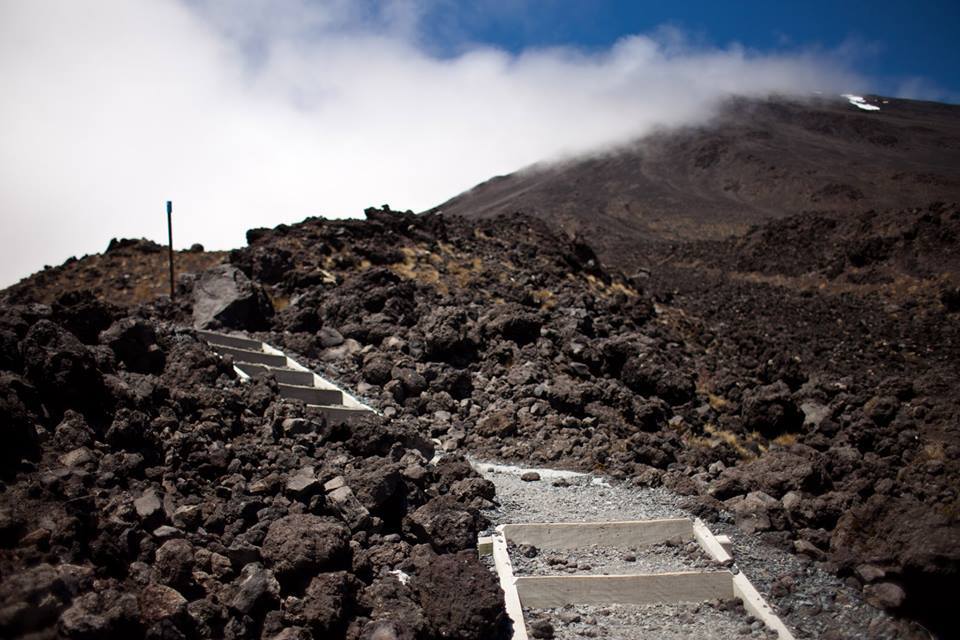 A built gravel-and-timber track climbing across black volcanic rock on the Tongariro Alpine Crossing